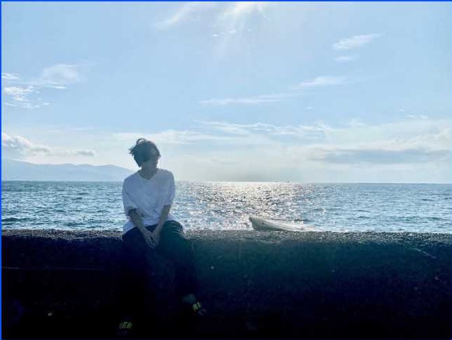 海辺に腰をかけ、風を受ける人物